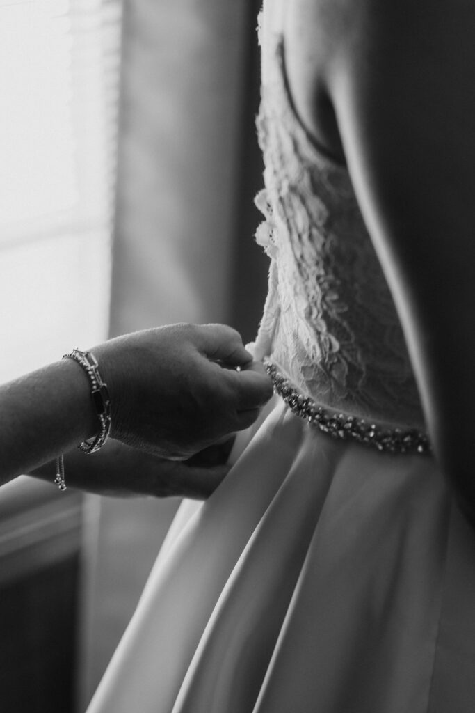 Mother helping bride zip dress, during bride getting ready