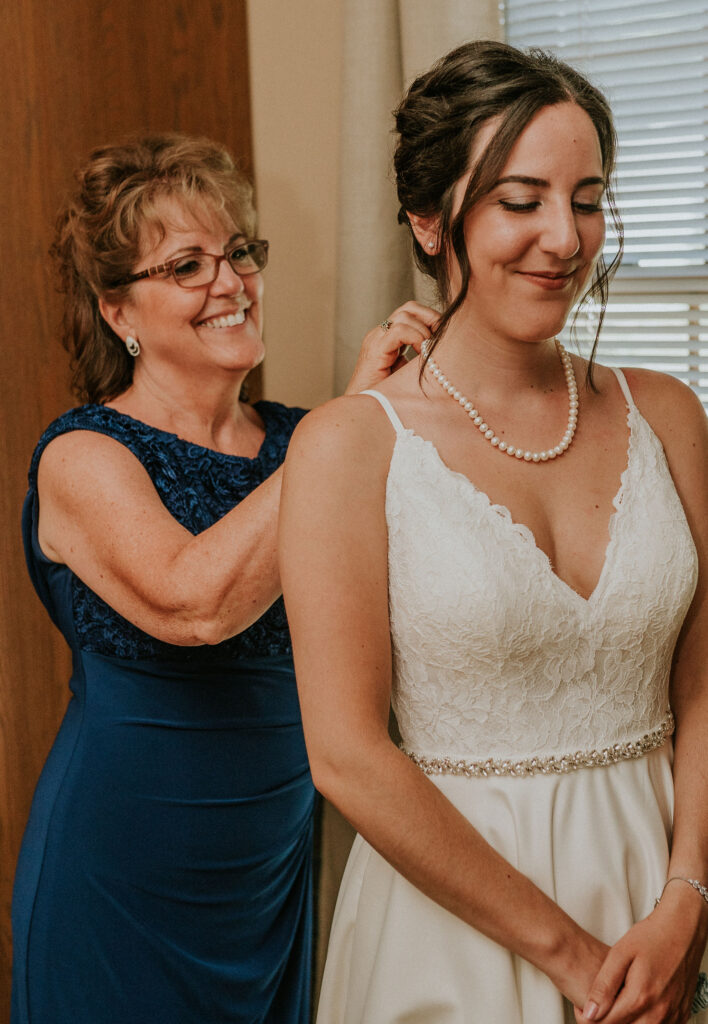 Mother helping bride put on necklace, during bride getting ready